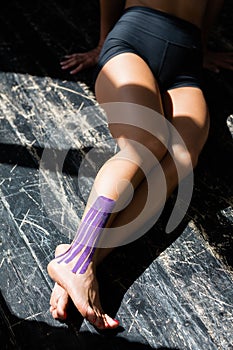 Close-up of female legs. A girl sits on the floor with a kinesiotherapy tape on the lower leg