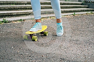 Close-up of female legs in jeans and sneakers riding a skateboard in the park