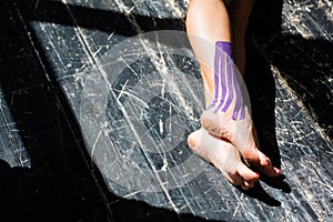 Close-up of female legs with purple kinesitherapy patch on ankle
