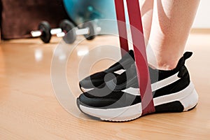 Close up female legs in sneakers doing exercises with fitness elastic bands at home during lockdown. Home workout. with