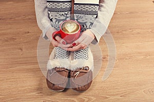 Close-up of female legs in warm socks with a deer, christmas presents, wrapping paper, decoration and cup of cappuccino top view.