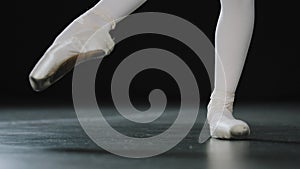 Close-up female legs in white tights and punts of ballet shoes doing dance exercises pulling stretching foot