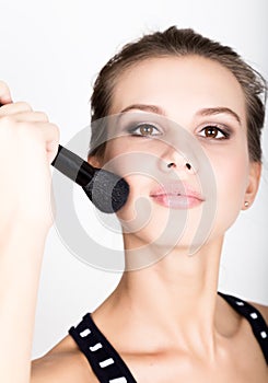 Close-up Female model applying makeup on her face. Beautiful young woman applying foundation on her face with a make up