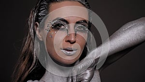 Close-up of a female model with silver skin and hands on a black background.