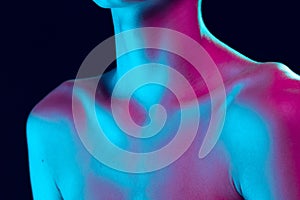 Close up female neck, collarbones and shoulders in pink neon light over dark background. Natural beauty, fitness, diet