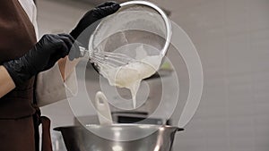 Close-up of a female pastry chef pouring whipped cream into a metal bowl.