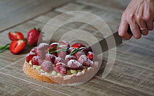 Close up of female pastry chef`s hand cuts  the delicious French strawberry cake