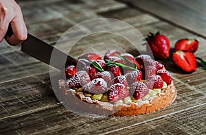 Close up of female pastry chef`s hand cuts  the delicious French strawberry cake