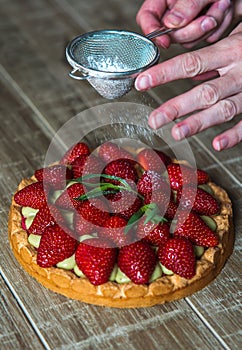 Close up of female pastry chef`s hand decorating  top of delicious French strawberry cake