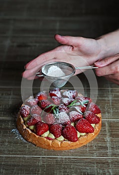 Close up of female pastry chef`s hand decorating  top of delicious French strawberry cake