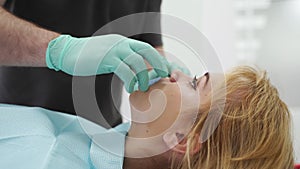 Close-up of female patient face. Dentist's hands taking off mouth expander after finishing UV teeth whitening in the