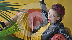 Close-up female portrait of glam rock style girl with dark pink hair and mohawk in yellow dress and black leather jacket