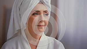 Close up female portrait middle-aged lady with towel on head in bathroom turn head to camera smiling 60s mature woman in