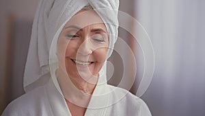Close up female portrait middle-aged lady with towel on head in bathroom turn head to camera smiling 60s mature woman in