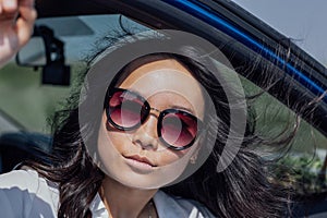 Close-up of a female portrait of a young attractive Asian woman in a car. Charming Korean in stylish sunglasses outdoors