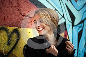 Close-up female portrait of young smiling girl with short blonde hair near the wall with graffiti. Youth culture, street