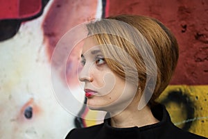 Close-up female portrait of young smiling girl with short blonde hair near the wall with graffiti. Youth culture, street