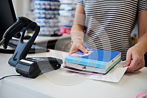 Close-up female seller standing at counter with barcode scanner, holding school stationery in the office supply store.