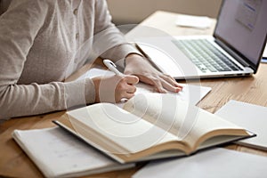 Close up female student writing down notes from opened textbook.