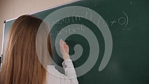 Close-up of a female student writing formulas on a blackboard in mathematics.