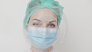 Close up of a female surgeon`s face, in medical cap and mask, winking at camera. Medical professional woman doctor nurse
