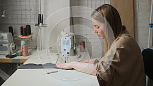 Close up of female tailor designer sews clothes, sitting in workshop at a table with a sewing machine. She enjoys creative work. F