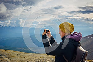 Close up female traveller on top of hill taking picture of beautiful mountain landscape on cloudy sunny day on smartphone. Freedom