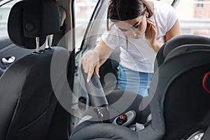 Close-up of female using portable vacuum cleaner in her car. Baby ca seat cleaning. Woman vacuuming seats. Dust and dirt