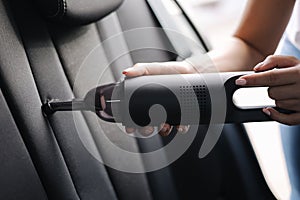 Close-up of female using portable vacuum cleaner in her car. Car interior cleaning. Woman vacuuming seats. Dust and dirt