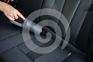 Close-up of female using portable vacuum cleaner in her car. Car interior cleaning. Woman vacuuming seats. Dust and dirt