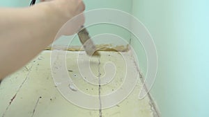 Close-up of female worker hand closes hole between wall and floor with silicone sealant caulking gun and putty knife