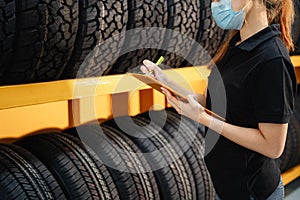 Close up female worker wear a mask to prevent the spread of corona virus or COVID-19 checking the stock of car tires at warehouse photo