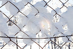 A close-up on an fence net with snow flakes frozen to it and the sun`s rays shining through the winter afternoon