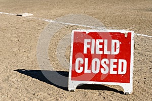 Close up of Field Closed sign on empty local baseball field, third base and baseline, on a sunny day