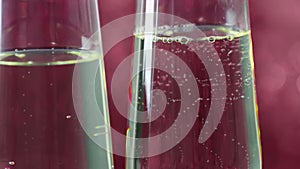 Close-up of filling flutes of champagne with golden bubbles against red bokeh background, concept of golden luxury holiday