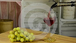 Close-up of filling a glass with red wine in slow motion. Pouring red wine into a glass. A bunch of grapes in the foreground