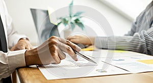 A close-up of a financial businessman holding a pen and pointing at the information sheet on his desk.