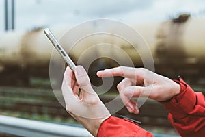 Close-up. Finger in front of a smartphone in a man`s hand. Against the background of railway cars with oil products tanks