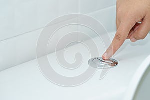 Close up of finger pushing a flush toilet button for cleaning. -