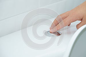 Close up of finger pushing a flush toilet button for cleaning. -