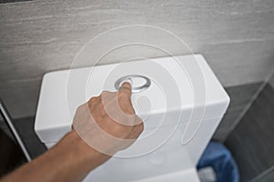 Close up of finger pushing a flush toilet button for cleaning a toilet.