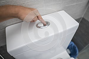 Close up of finger pushing a flush toilet button for cleaning a toilet.