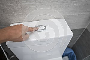 Close up of finger pushing a flush toilet button for cleaning a toilet.