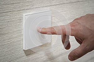 close-up finger turns on the light on the touch switch. A white modern light switch on a white wall. modern design