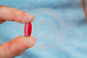 Close-up of fingers holding a red pill.