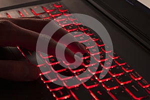 Close up of fingers typing on glowing red backlight keys on a computer keyboard. in the dark. Computer hacker, internet fraud or s