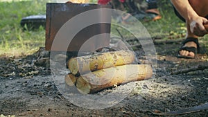 Close-up of firewood and an axe at a campsite with a burning fire pit in the background. Camping preparation and fire