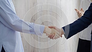 Close-up of a firm handshake between two professionals with a colleague applauding in the background