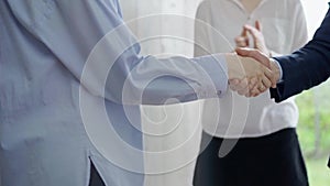 Close-up of a firm handshake between two professionals with a colleague applauding in the background