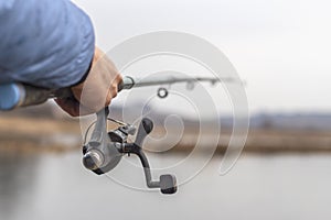 Close up of fisherman hand with fishing rod and reel on the lake.
